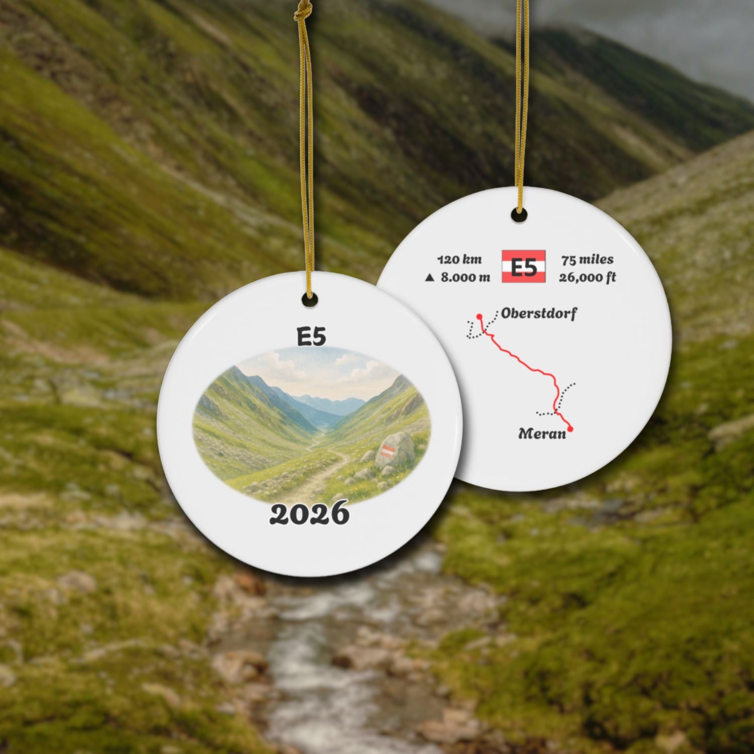 E5 Oberstdorf - Meran ceramic ornament with watercolor landscape shown front and back in front of trail landscape.