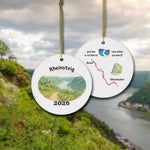 Rheinsteig ceramic ornament with watercolor landscape shown front and back in front of trail landscape.