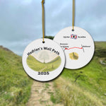 Hadrian's Wall Path ceramic ornament with watercolor landscape shown front and back in front of trail landscape.