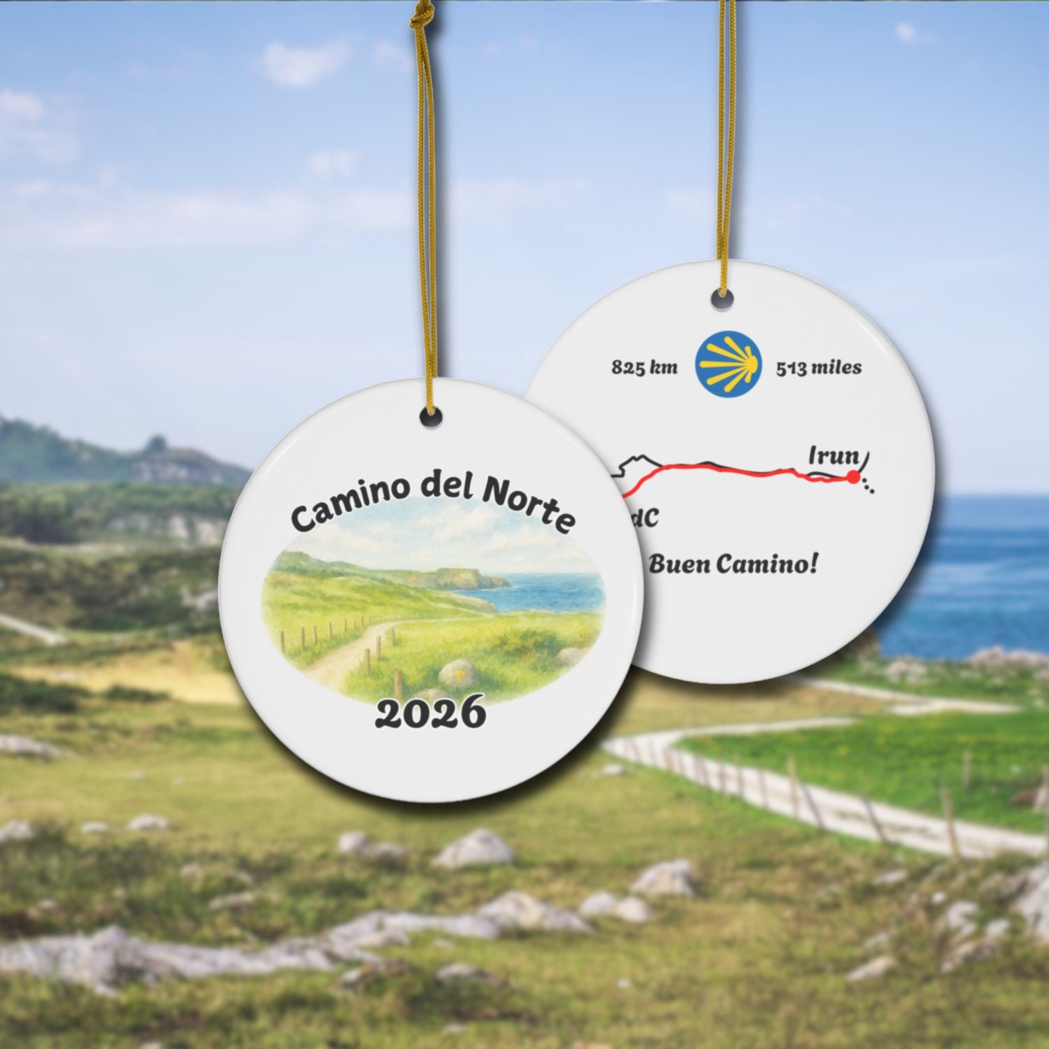 Camino del Norte ceramic ornament with watercolor landscape shown front and back in front of trail landscape.