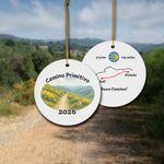 Camino Primitivo ceramic ornament with watercolor landscape shown front and back in front of trail landscape.