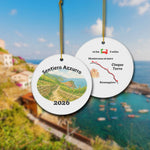Sentiero Azzurro ceramic ornament with watercolor landscape shown front and back in front of trail landscape.