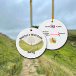 Front and back view of a round ceramic ornament with “Hadrian’s Wall Path 2025” and a gentle watercolor scene of the Sycamore Gap with and without the Sycamore. The back shows a trail map with 135 km / 84 miles and a Hadrians Wall miniature watercolor.